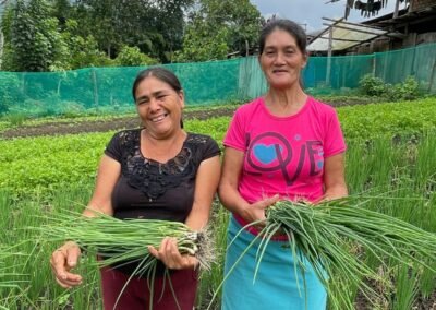 Dos socias de AMEP sonrientes sostienen cebollas cosechadas de su biohuerto